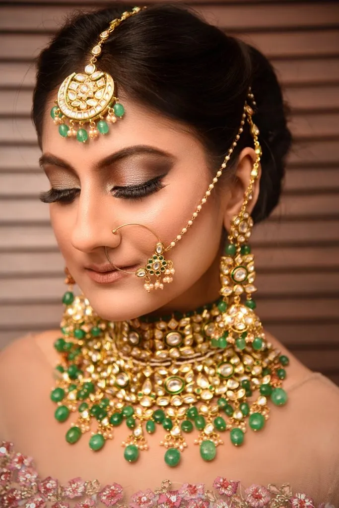 Bridal gold jewellery with kundan and emerald-style stones, worn as a maang tikka, nath and choker
